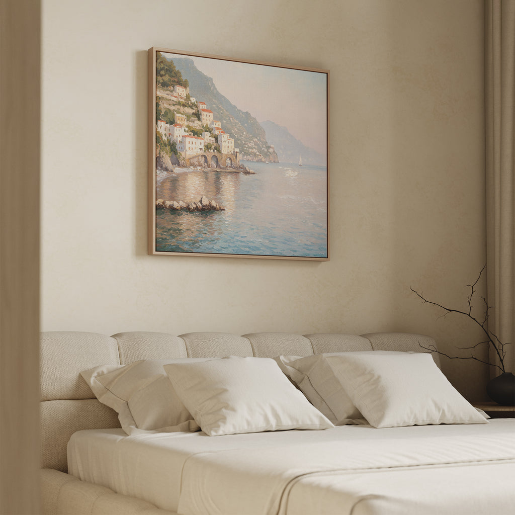 A minimal, modern bedroom features a beige bed, white pillows, and the Mediterranean Dreams Canvas Art - Square of a coastal village above the headboard. Soft natural light filters through a curtain on the right, enhancing the serene home decor.
