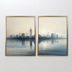 The Metropolitan Dawn - Set of 2 features two framed city skyline artworks side by side, showcasing tranquil urban scenes at sunrise or sunset with tall buildings reflected in calm water and soft blue and beige tones for a serene look.