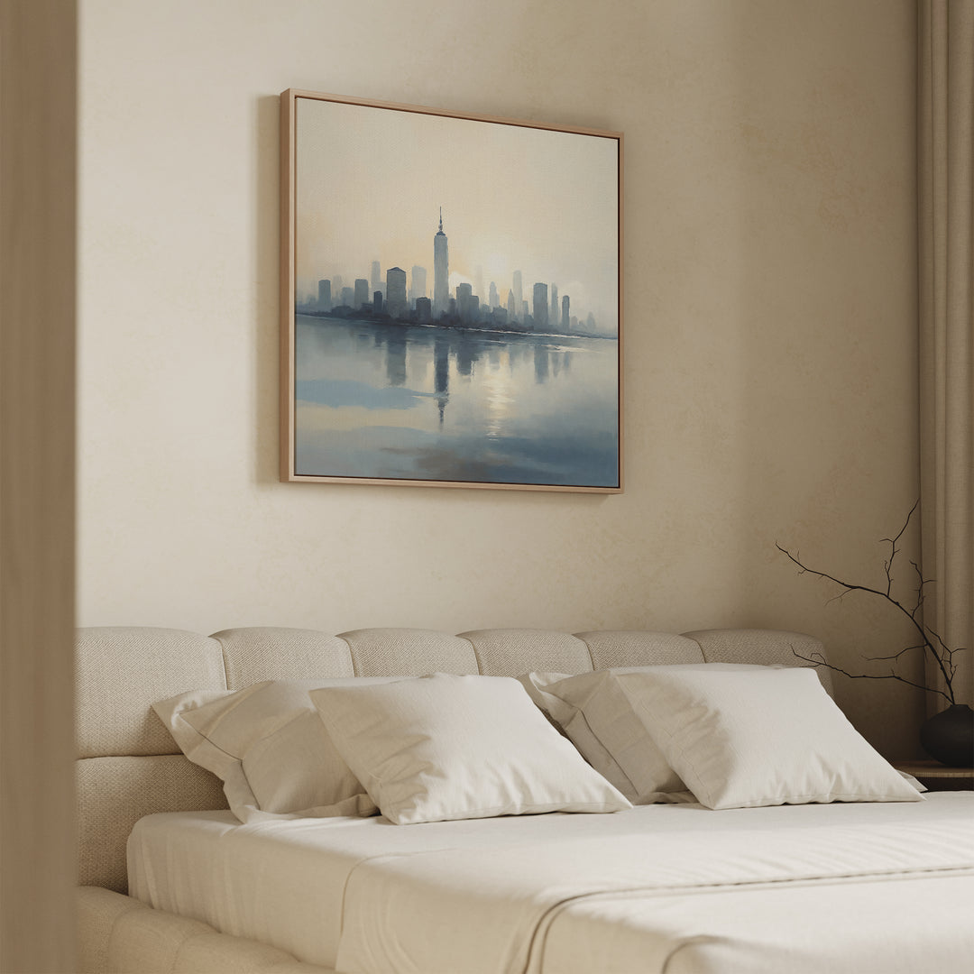 A beige-toned bedroom features a neatly made bed with four white pillows and the Metropolitan Dawn Canvas Art - Square, showcasing a city skyline, hanging above the headboard. A vase with bare branches sits on the nearby nightstand.