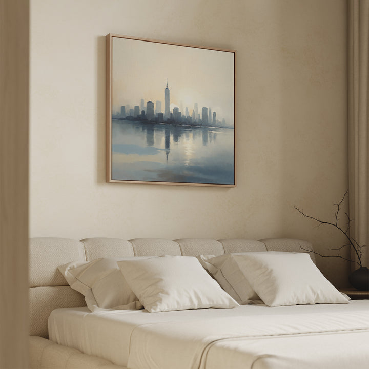 A beige-toned bedroom features a neatly made bed with four white pillows and the Metropolitan Dawn Canvas Art - Square, showcasing a city skyline, hanging above the headboard. A vase with bare branches sits on the nearby nightstand.