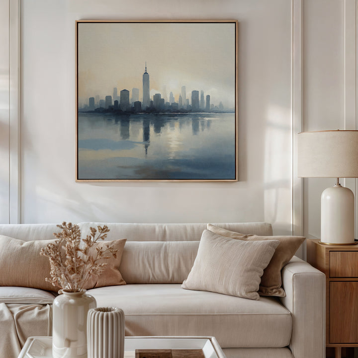 A modern living room features a beige sofa, neutral cushions, a wooden side table with a lamp, dried flowers in a vase, and the Metropolitan Dawn Canvas Art - Square above the couch. The minimalist decor creates a calming atmosphere.