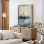 A modern living room with soft, neutral furniture features the Metropolitan Dawn Canvas Art - Vertical, showcasing an urban skyline in blue and yellow. A light wooden cabinet, beige vases, books, and a potted plant complete this tranquil minimalist space.