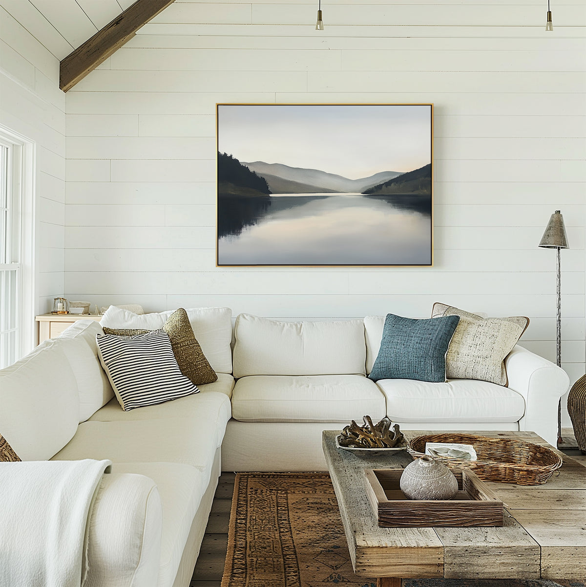 A cozy living room with a white sectional sofa, assorted pillows, a rustic wooden coffee table, and the Mirror Valley Canvas Art - Horizontal in calming natural hues hanging on a white shiplap wall.