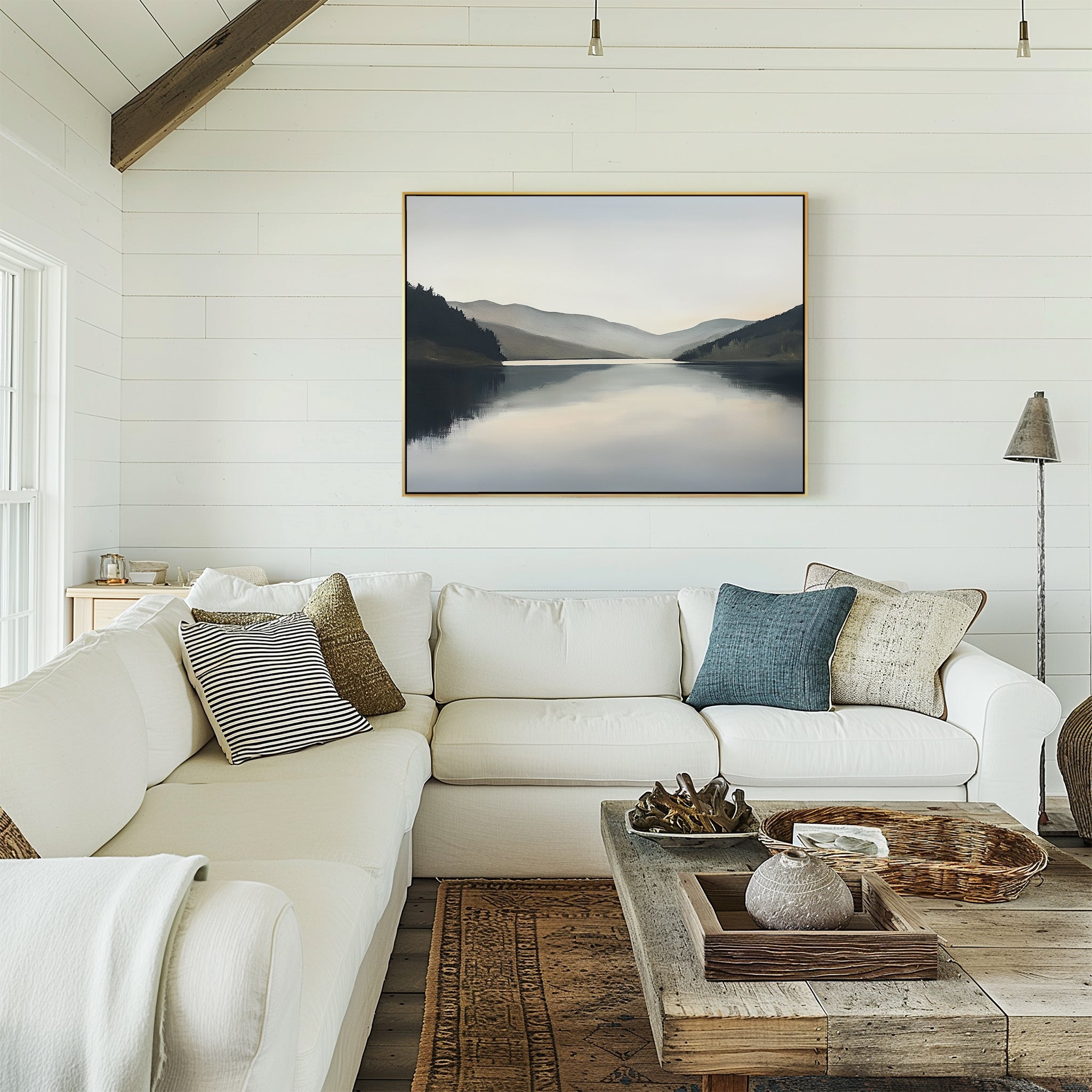 A cozy living room with a white sectional sofa, assorted pillows, a rustic wooden coffee table, and the Mirror Valley Canvas Art - Horizontal in calming natural hues hanging on a white shiplap wall.