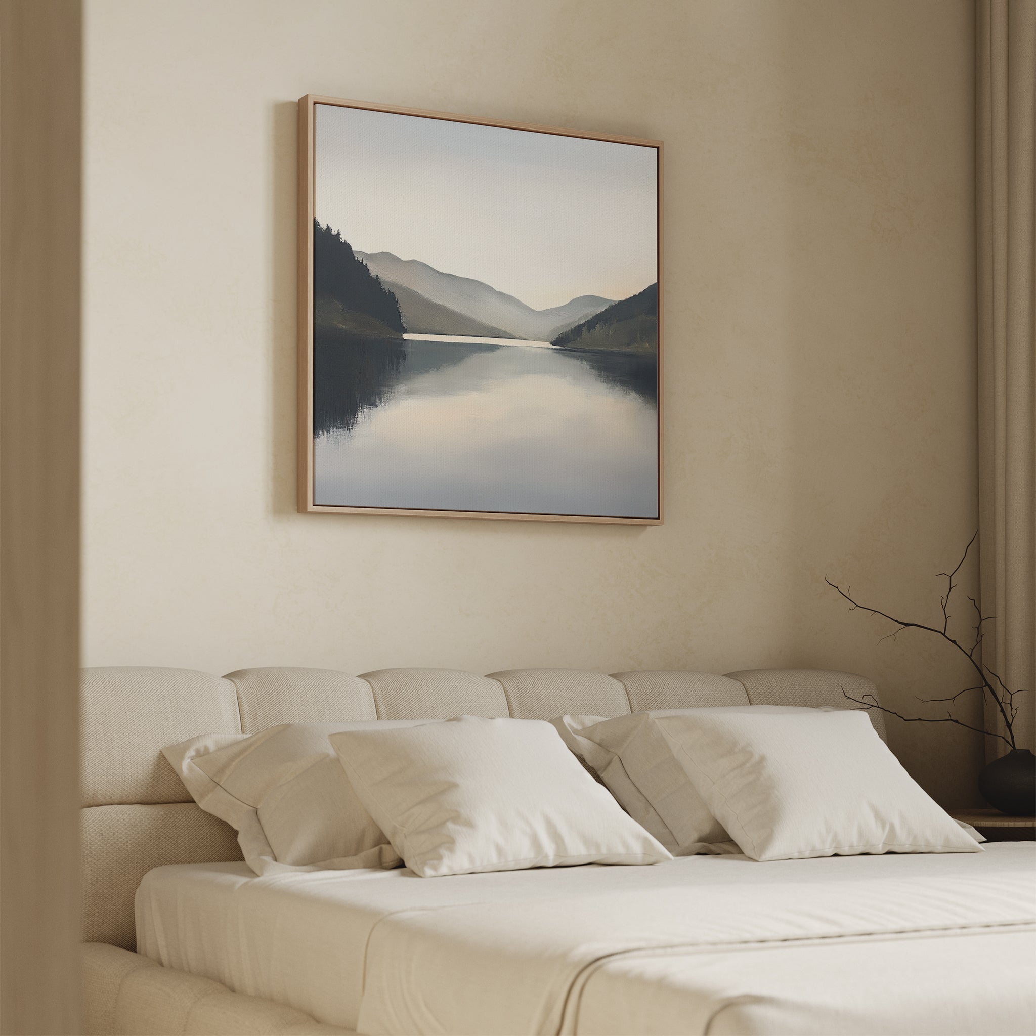 A minimalist bedroom features a beige upholstered bed with white bedding and four pillows. Above the bed, the Mirror Valley Canvas Art - Square brings serene mountain landscape wall art to the space. A bare branch decorates the bedside table.