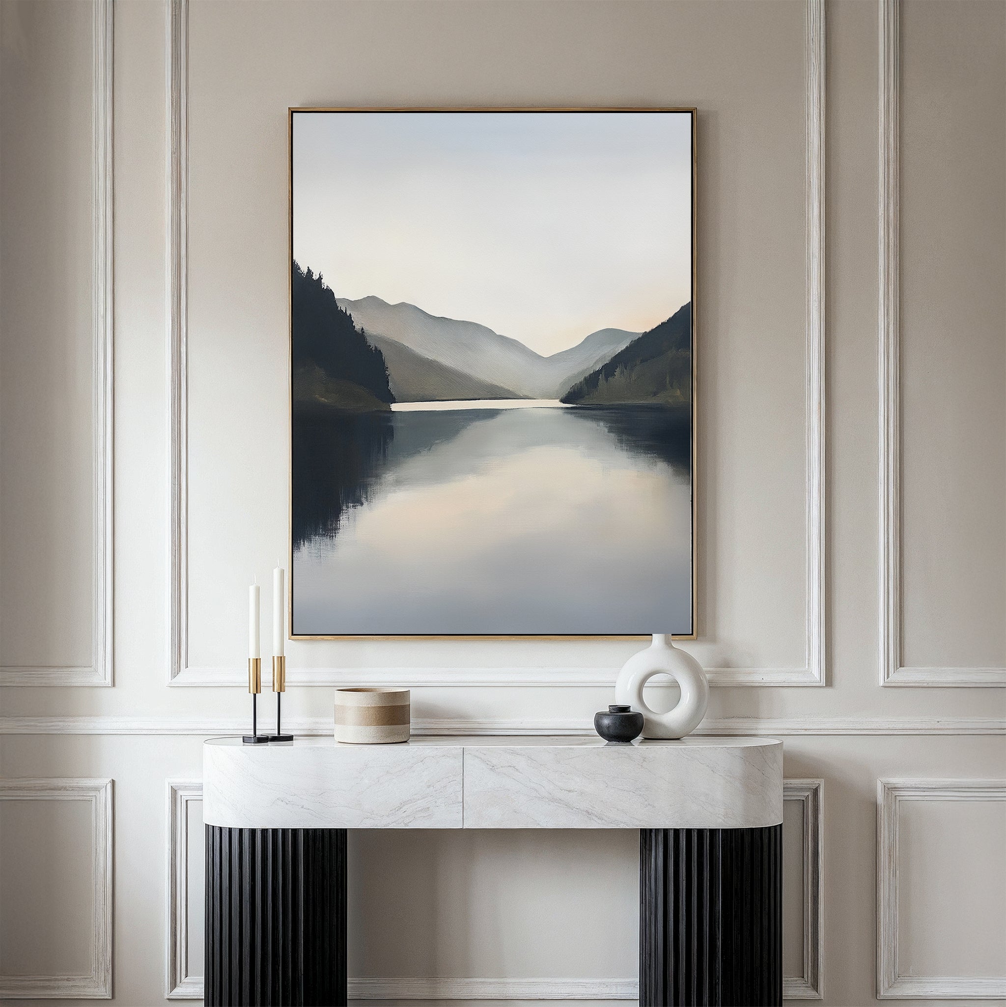 The Mirror Valley Canvas Art - Vertical, featuring a serene lake and mountains, hangs above a light console table adorned with candles, a bowl, and an abstract sculpture, adding effortless Nordic style to your space.