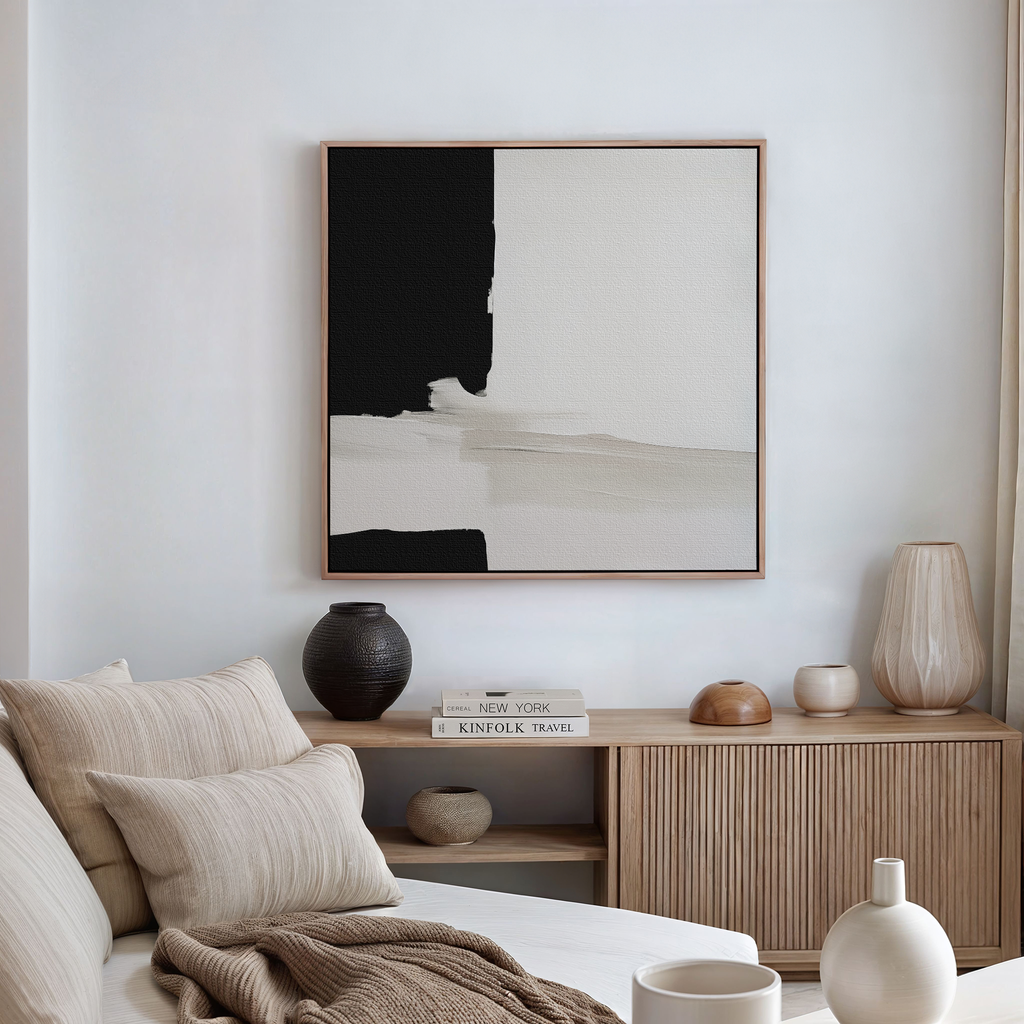 A minimalist living room with a beige sofa, neutral cushions, wooden sideboard, decorative vases, stacked books, and Monochrome Harmony Abstract Canvas Art—a striking black-and-white piece serving as captivating modern wall decor.