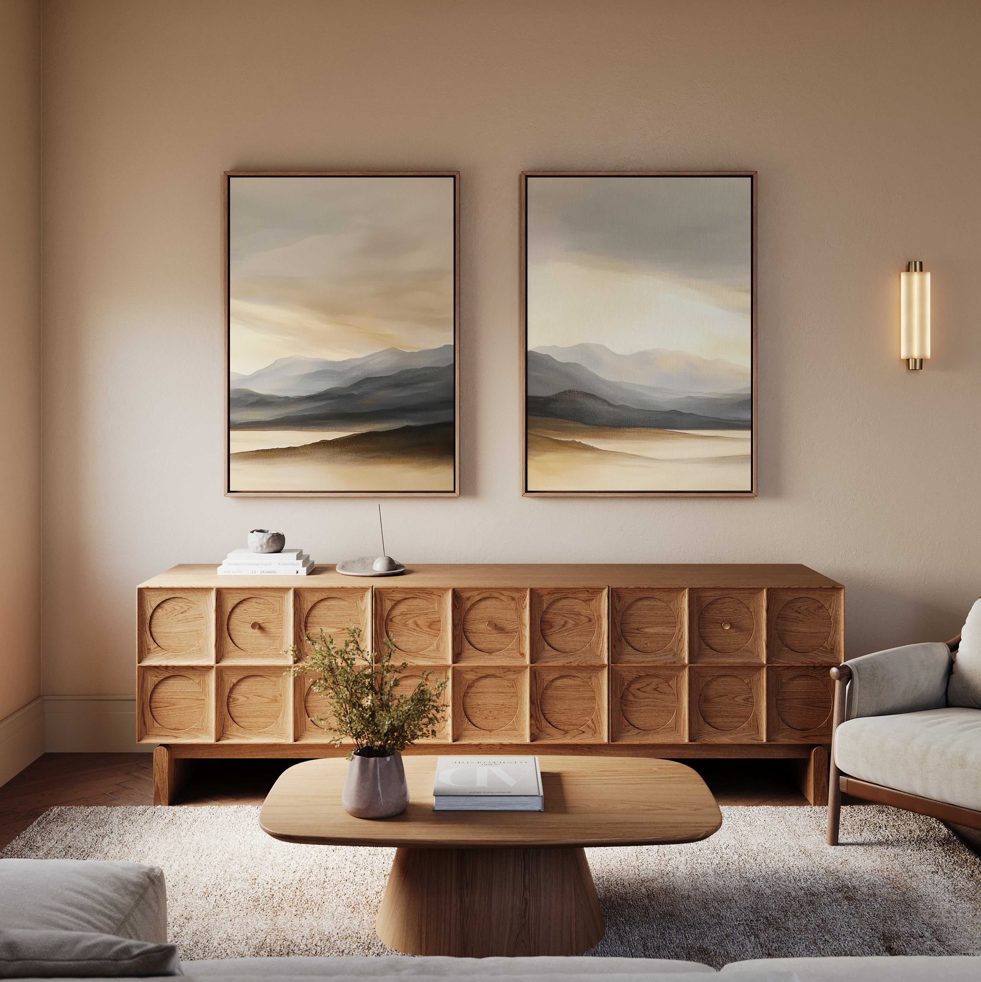 A modern living room featuring a wooden coffee table, textured sideboard, plush armchair, wall sconce, a vase with greenery on the table, and the Mountain Reverie - Set of 2 serene art prints displayed above.