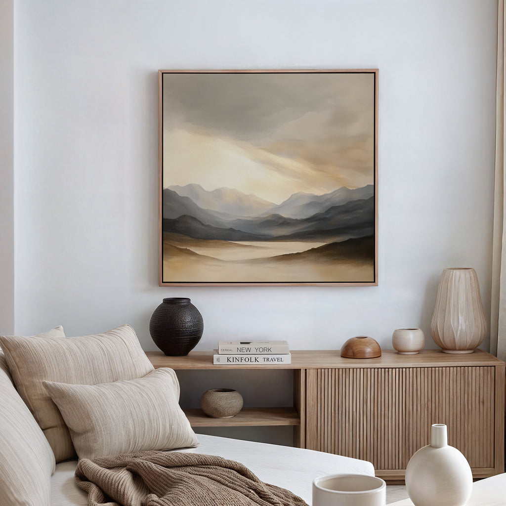 A serene living room with neutral decor, a beige couch with cushions, a wooden sideboard holding vases and books, and the Mountain Reverie Canvas Art - Square hanging on the white wall.