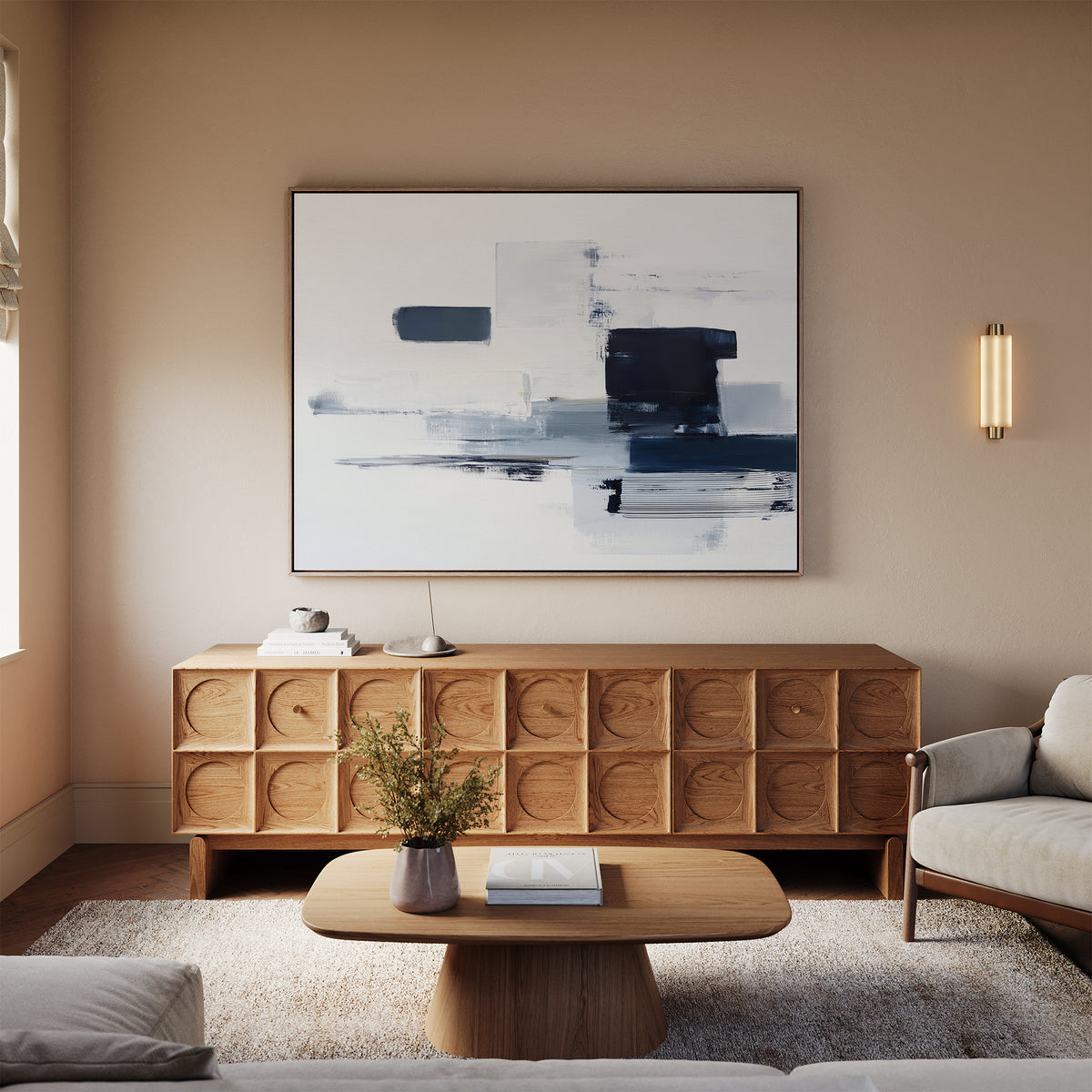 A modern living room with beige walls, a wooden credenza, a light sofa, a wooden coffee table with a vase and book, warm neutral tones, and the Navy Brushwork Canvas Art - Horizontal as navy abstract wall art.