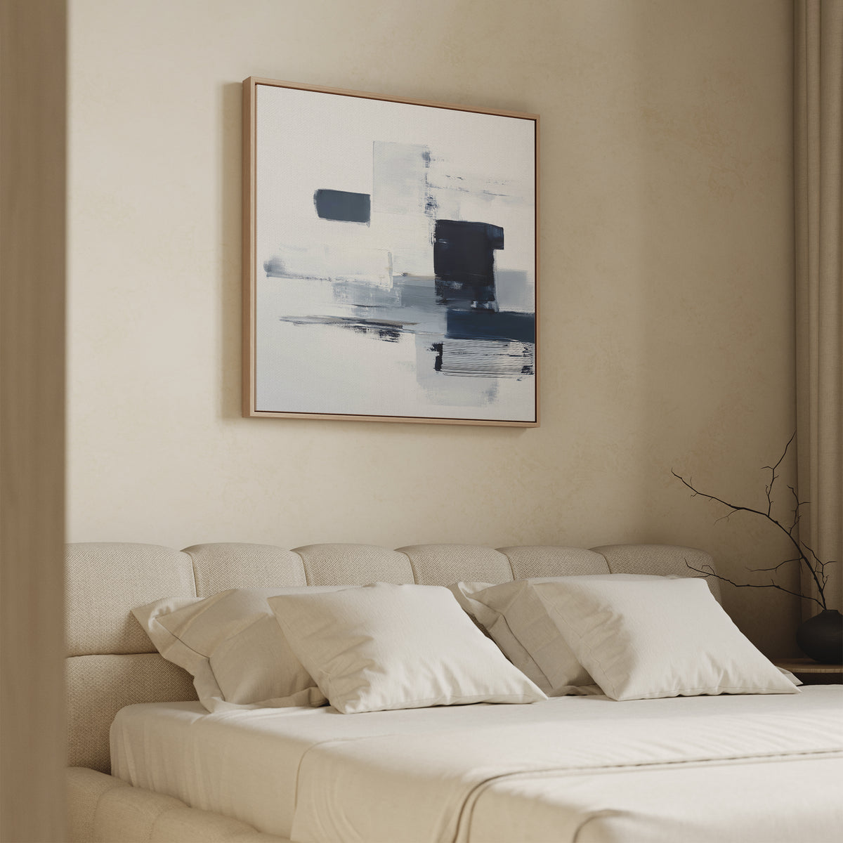 A modern bedroom features a beige upholstered bed with white bedding and four pillows. The Navy Brushwork Canvas Art - Square hangs above, while a bare branch in a vase on the bedside table completes the minimalist decor.