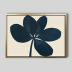 Navy Clover Canvas Art - Horizontal features a dark blue abstract five-petal flower with stem on beige canvas, framed in slim gold, against a light gray wall. Ideal for modern minimalist decor.