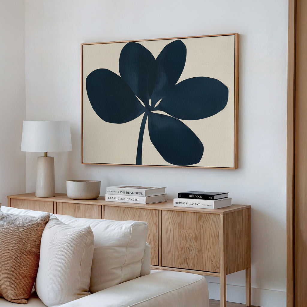 A modern living room featuring a light wood sideboard, white table lamp, decorative bowls, stacked books, and the Navy Clover Canvas Art - Horizontal above a white sofa with neutral cushions.
