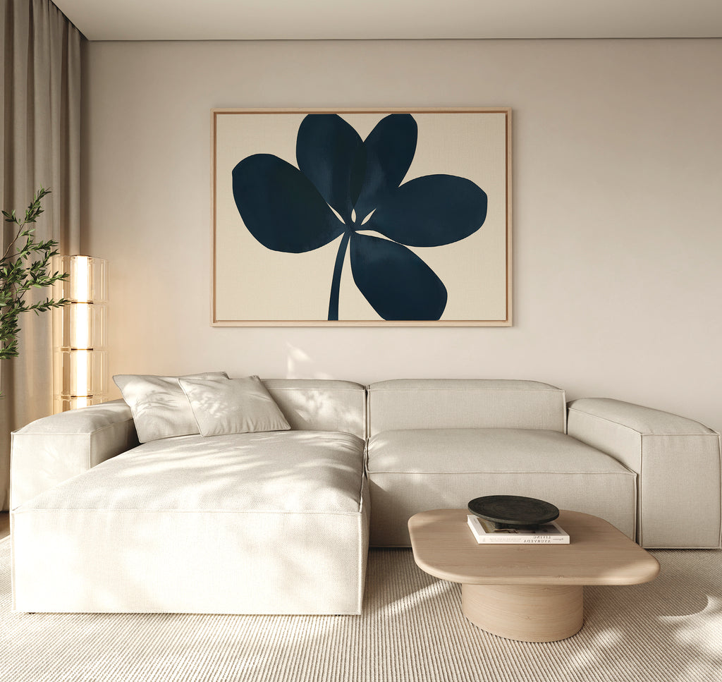 A modern living room with a light beige sectional, a low wooden coffee table, and minimalist wall decor featuring the Navy Clover Canvas Art - Horizontal. A tall plant and sheer curtains add a cozy touch.