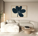 A modern living room with a light beige sectional, a low wooden coffee table, and minimalist wall decor featuring the Navy Clover Canvas Art - Horizontal. A tall plant and sheer curtains add a cozy touch.