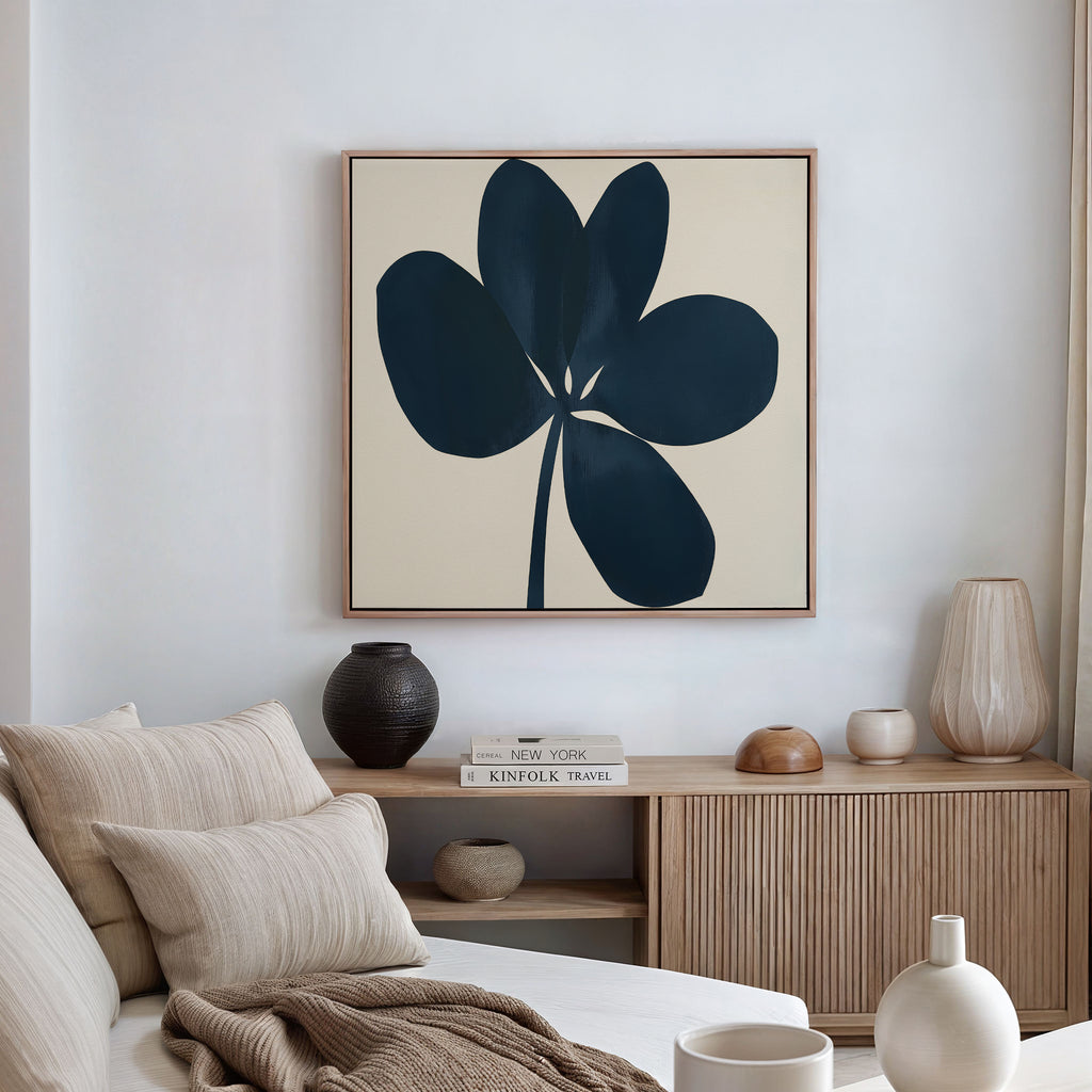 A modern living space featuring a beige sofa, striped cushions, a wooden sideboard with vases, and the Navy Clover Canvas Art - Square as minimalist botanical wall art on the wall.