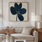 A neutral-toned living room with a beige sofa, light cushions, and a side table with a cream lamp. Above the sofa hangs the Navy Clover Canvas Art - Square, featuring a bold abstract navy flower on a light background.