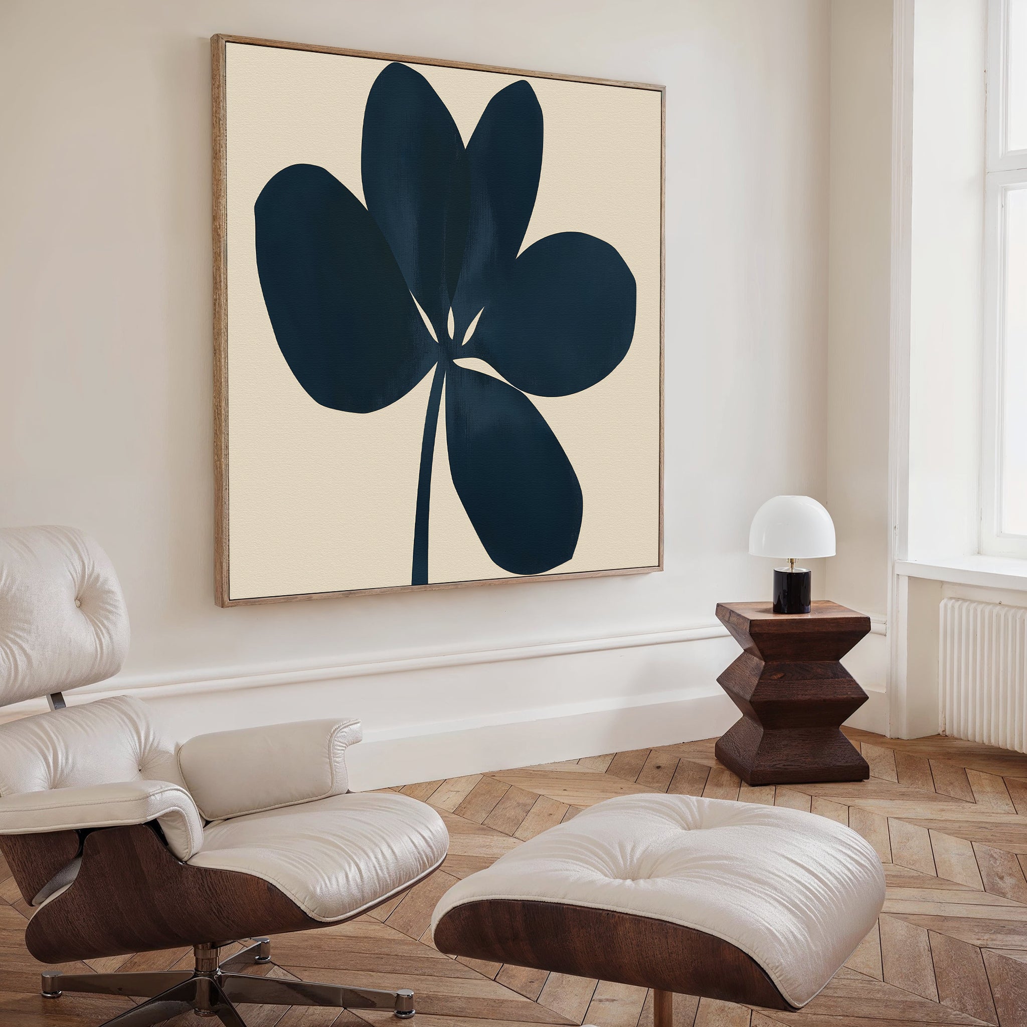 A modern living room featuring a white leather lounge chair and ottoman, a geometric wooden side table with a small white lamp, and the Navy Clover Canvas Art - Square as bold minimalist wall decor.