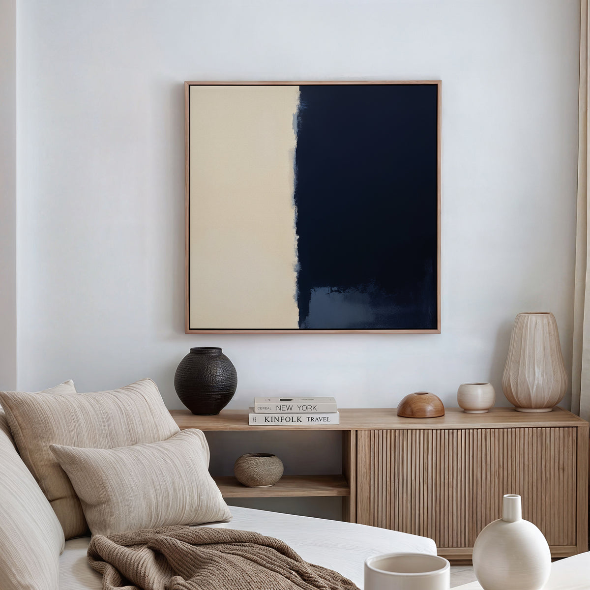 A modern living room with a beige sofa, neutral cushions, and a wooden sideboard displaying vases, bowls, and books. The Navy Division Canvas Art - Square featuring abstract blocks hangs on the white wall.