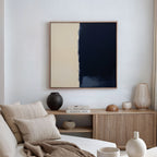 A modern living room with a beige sofa, neutral cushions, and a wooden sideboard displaying vases, bowls, and books. The Navy Division Canvas Art - Square featuring abstract blocks hangs on the white wall.