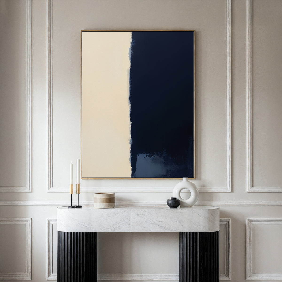 A minimalist room with cream walls, a marble console table, and modern accents—candles, a round sculpture, and a black bowl. Above the console hangs the Navy Division Canvas Art - Vertical in beige and dark blue tones.
