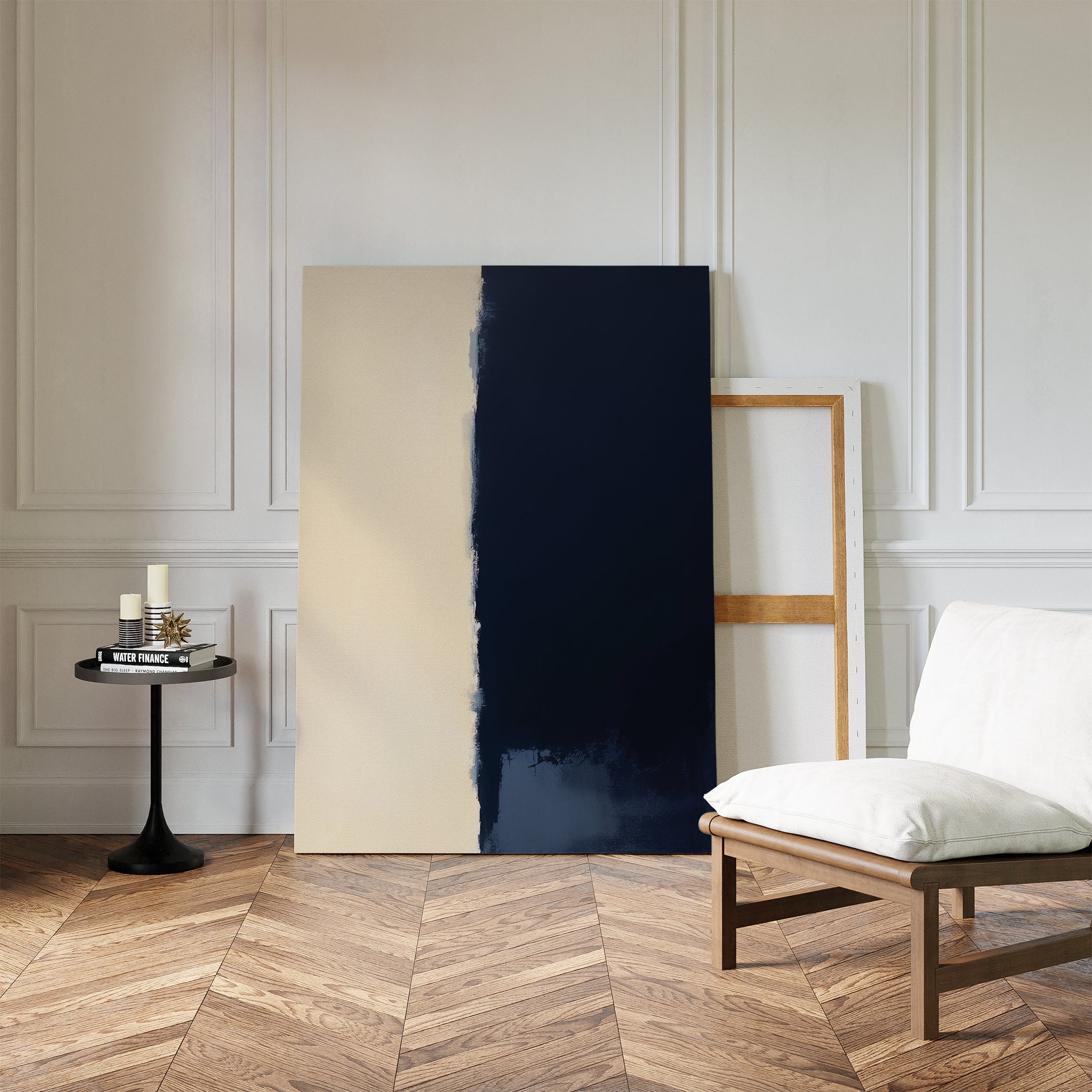 A modern room with herringbone wood floors, a white cushioned chair, a small black side table with candles and books, and the Navy Division Canvas Art - Vertical leaning against a white paneled wall creates an air of modern elegance.