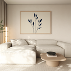 A modern living room with a light beige sectional, wooden coffee table, and the Navy Stem Canvas Art featuring blue leaves. Natural light streams through sheer curtains on the left.