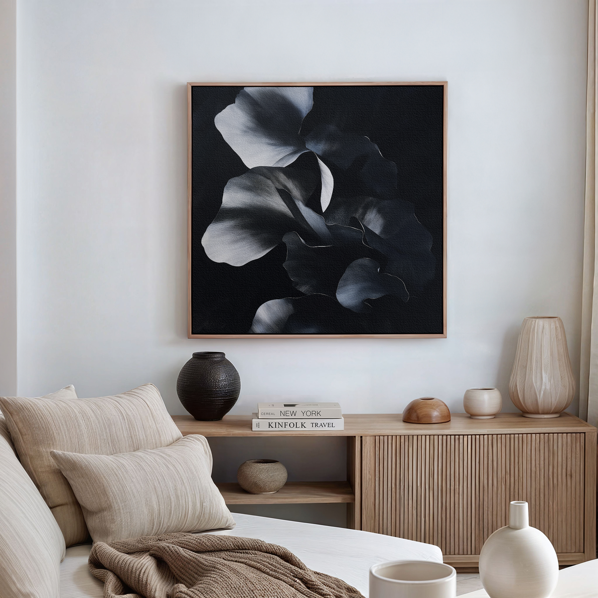 A minimalistic living room with a cream sofa, neutral pillows, a light wood sideboard with vases, books, and a tray, and Nocturnal Bloom Abstract Canvas Art as striking modern wall art.