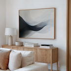 A modern living room with a light wood sideboard, beige sofa, table lamp, books, and the Rippling Vista Abstract Canvas Art in gray and white above the sideboard creates an atmosphere of modern elegance.