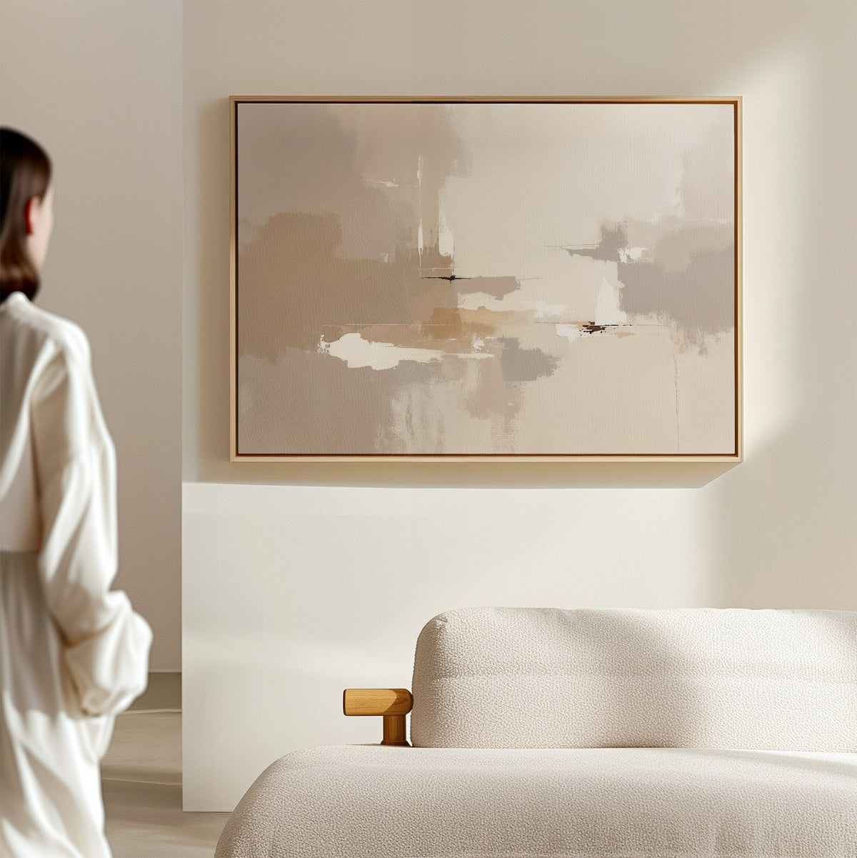 A person stands in a minimal, light-filled room with the Neutral Territory Canvas Art - Horizontal mounted above a textured cream sofa, creating a contemporary, modern look with neutral tones.