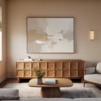 A modern living room features the Neutral Territory Canvas Art - Horizontal above a wooden sideboard, with a beige sofa, minimalist decor, a wooden coffee table topped with books and flowers, and a textured neutral-toned rug.