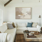 A cozy living room features a white sectional sofa, assorted pillows, a rustic wooden coffee table with decor, and the Neutral Territory Canvas Art - Horizontal adding contemporary elegance to the white shiplap wall in soft natural light.