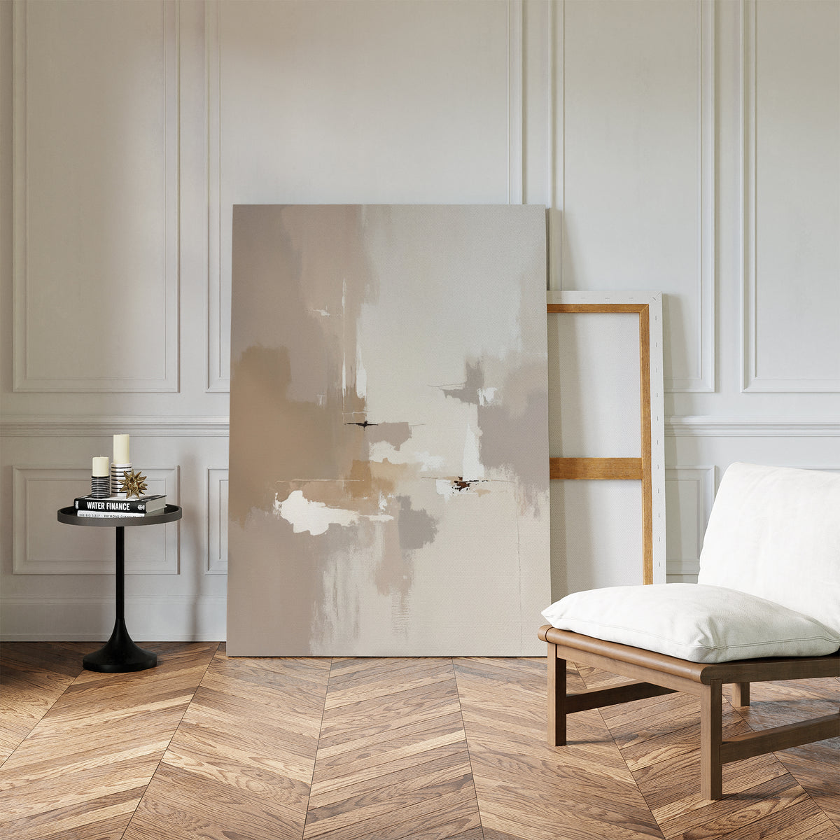 A modern living room with light wood herringbone floors, a white cushioned chair, a round black table with candles and books, and two Neutral Territory Canvas Art - Vertical pieces leaning against a white paneled wall.