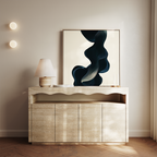 A modern sideboard with a wavy design displays a table lamp, two candles, and the Nocturnal Wave Abstract Canvas Art featuring dark, flowing shapes in a minimalist neutral-toned living room.