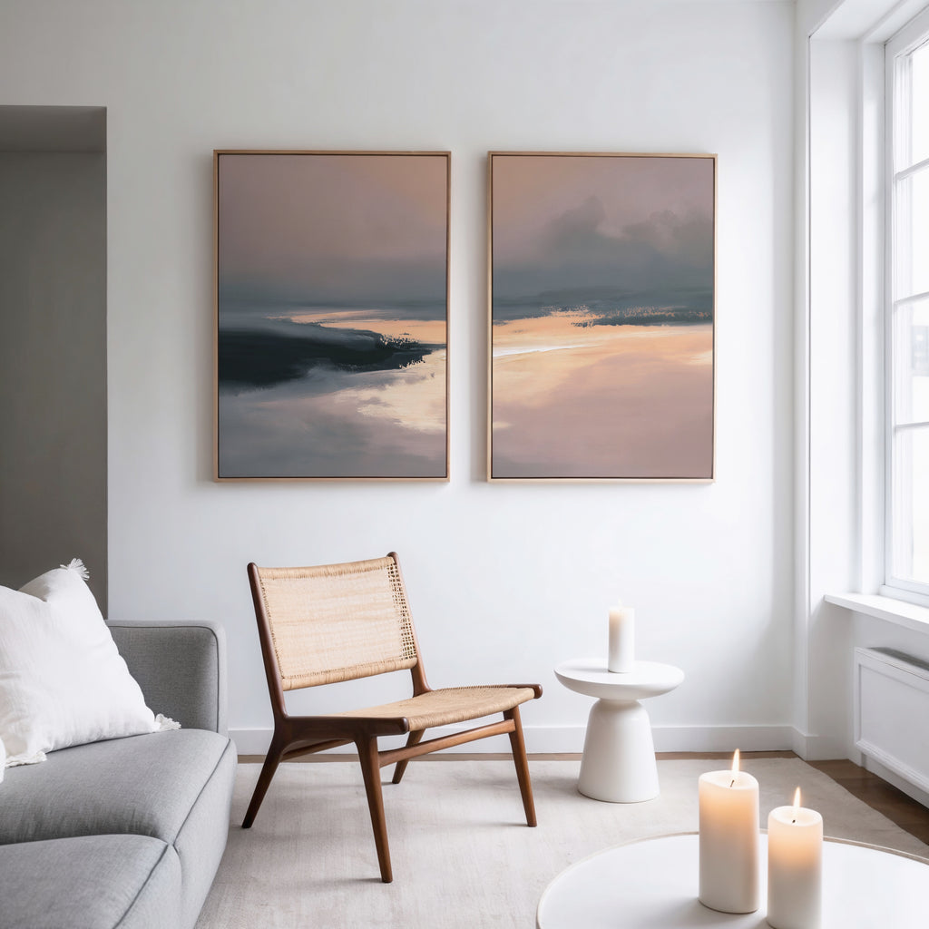 A modern living room with a wooden chair, small round table, lit candles, light gray sofa, and the Nordic Fjord - Set Of 2 abstract landscape wall art on a white wall by a large window.