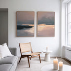 A modern living room with a wooden chair, small round table, lit candles, light gray sofa, and the Nordic Fjord - Set Of 2 abstract landscape wall art on a white wall by a large window.