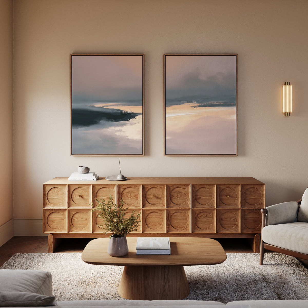 A cozy living room featuring a wooden sideboard, a coffee table with a book and vase of flowers, peaceful wall art above a beige sofa, and the Nordic Fjord - Set Of 2 abstract paintings—perfect for Nordic-inspired decor.
