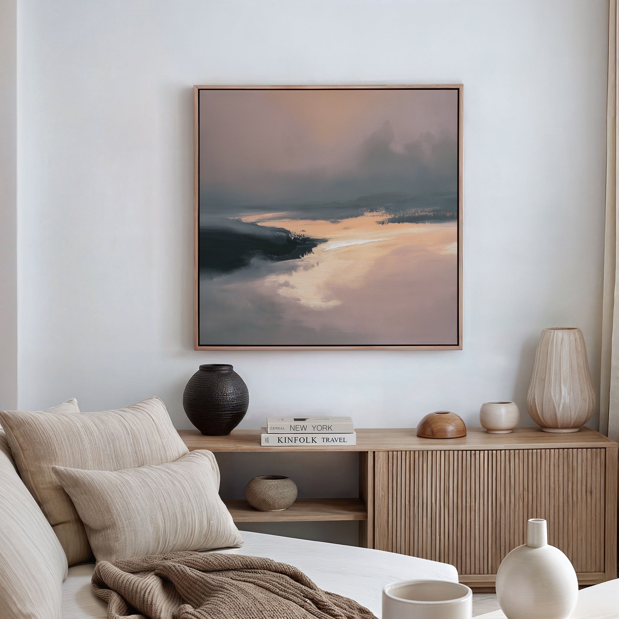 A modern, minimalist living room features a beige sofa, neutral cushions, wood sideboard with stacked books and decorative vases, and the Nordic Fjord Canvas Art - Square in soft earth tones as the focal wall décor.