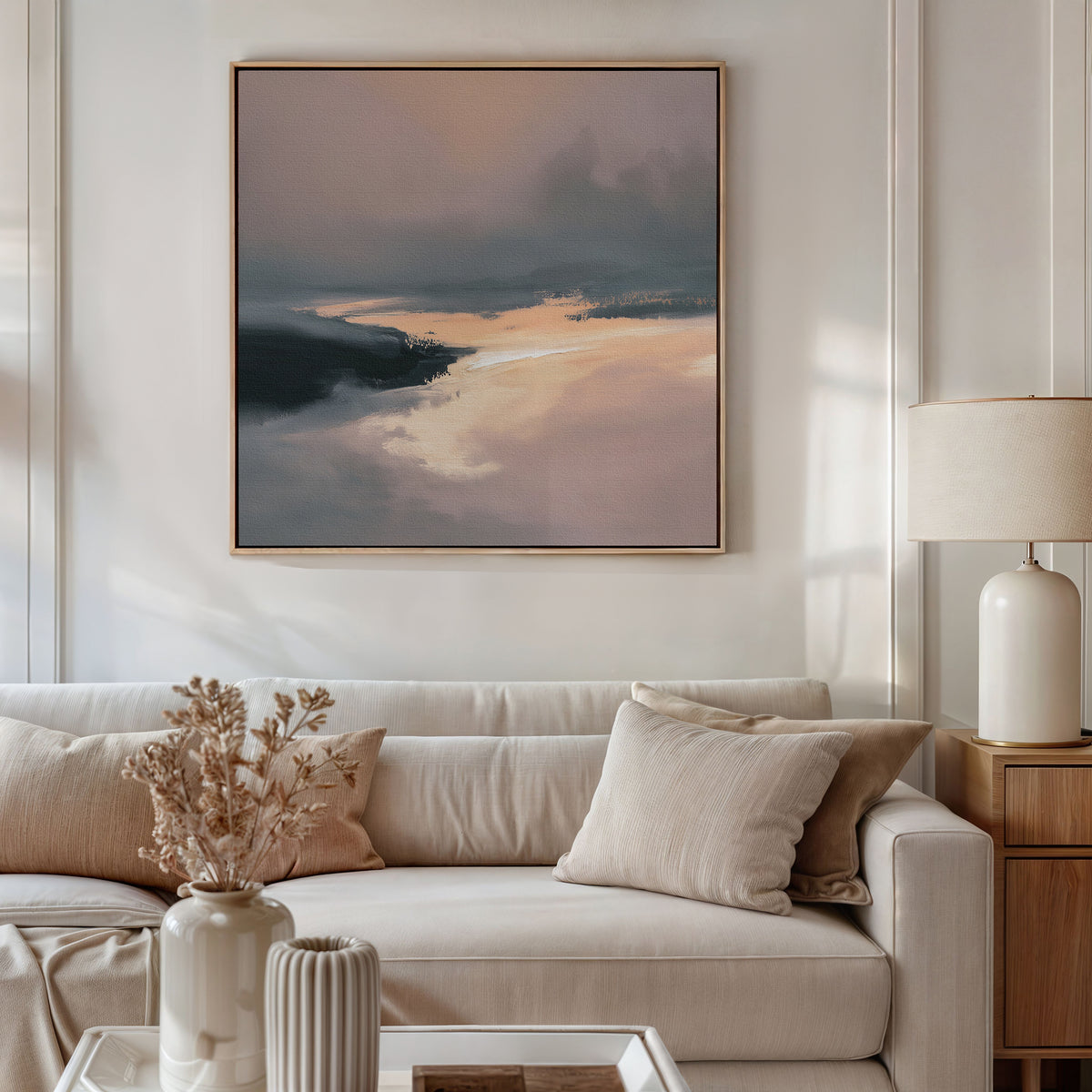 A modern living room with a beige sofa, matching cushions, a side table with a white lamp, dried flowers in a vase, and the Nordic Fjord Canvas Art - Square in muted tones hanging above the sofa.