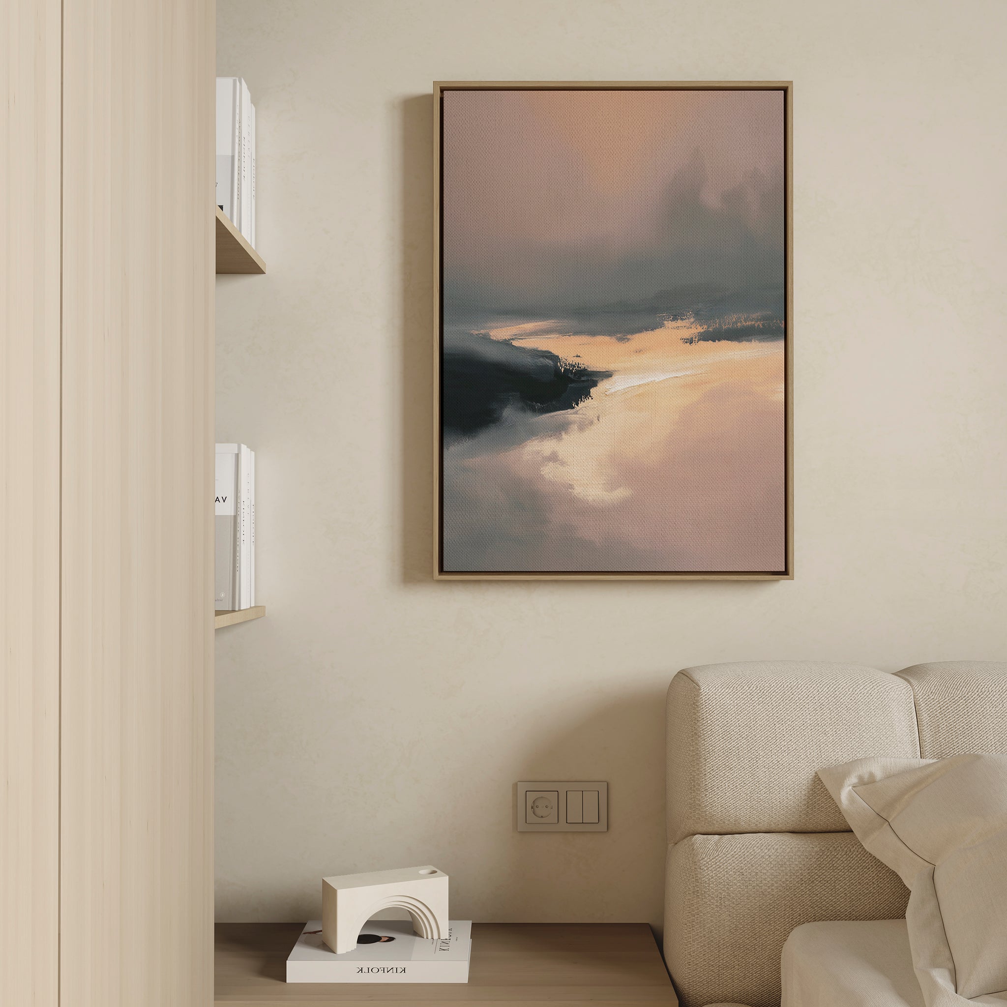 A modern living room features a beige sofa, a small shelf with books and decor, and the Nordic Fjord Canvas Art - Vertical, a framed landscape print in warm and dark tones displayed on a light-colored wall.