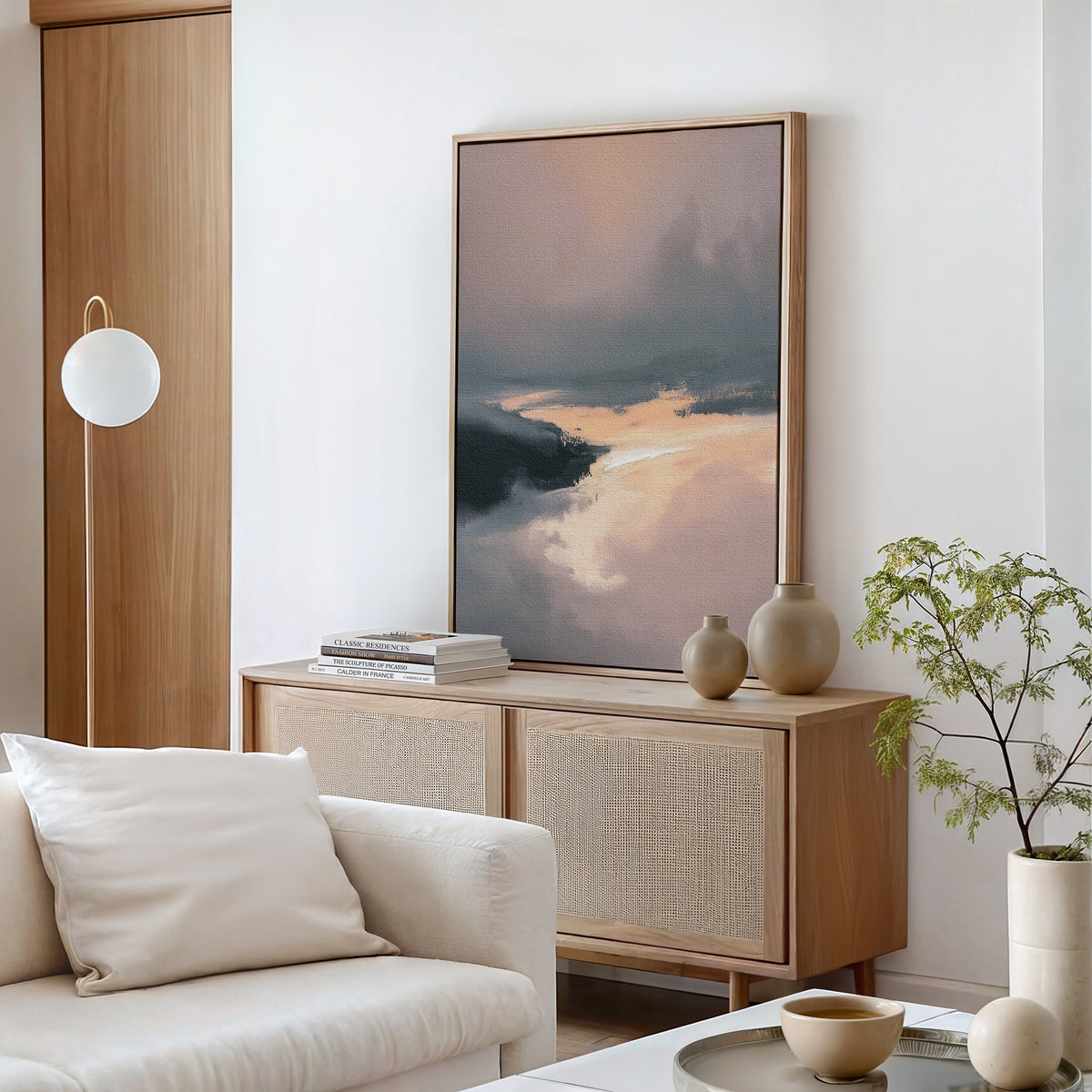 Minimalist living room featuring a light wood sideboard, Nordic Fjord Canvas Art - Vertical on the wall, neutral ceramics, small potted plant, soft beige armchair, and a globe lamp mounted beside the wooden door.