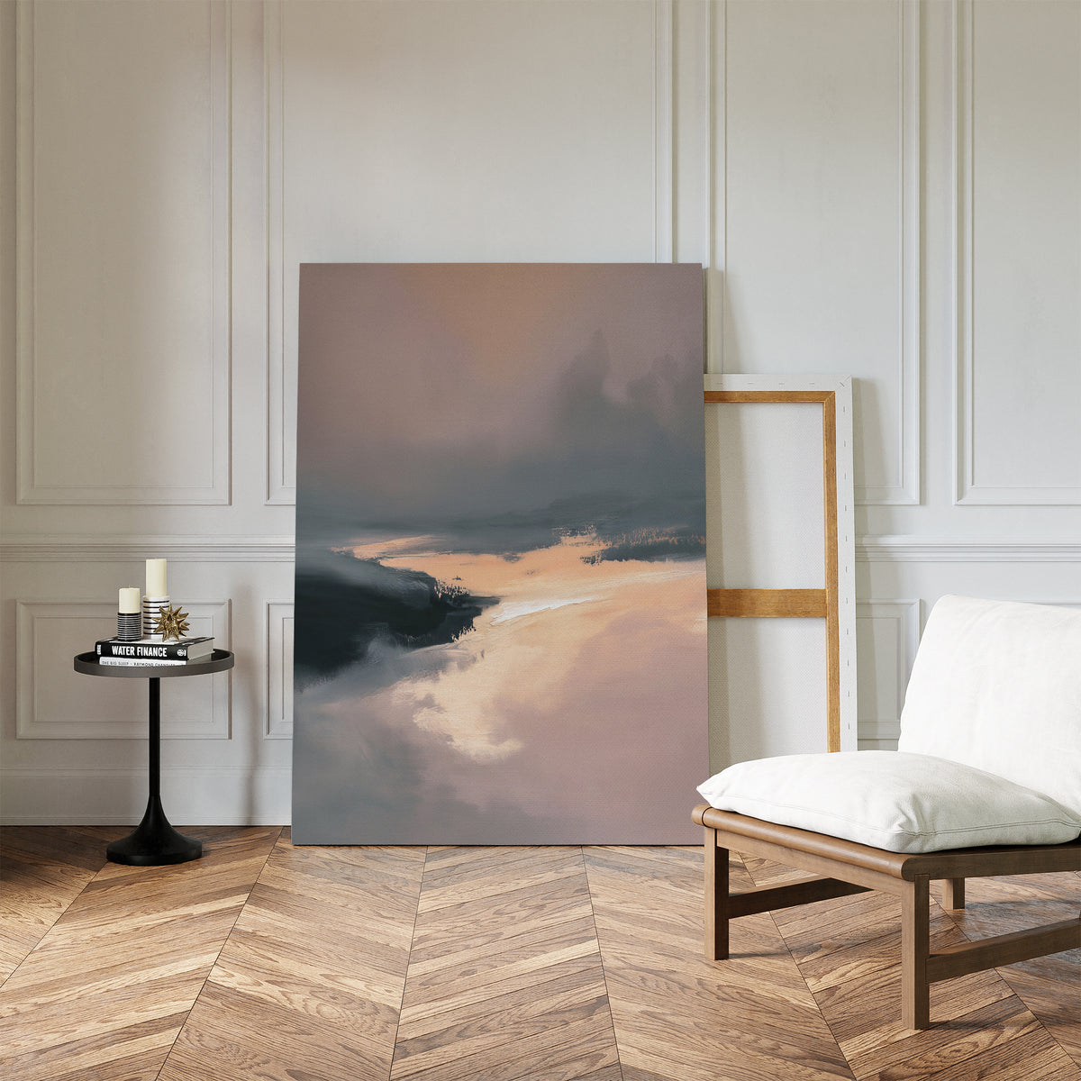 The Nordic Fjord Canvas Art - Vertical rests against a white paneled wall beside an empty wooden frame, while a cushioned chair and a small round table with candles and books sit on the herringbone wood floor.