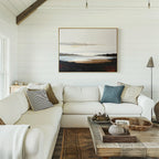 A cozy, modern living room features a white sectional sofa with throw pillows, a rustic wooden coffee table, and the Nordic Waters Canvas Art - Horizontal displayed on a white shiplap wall as natural light streams in from the left.