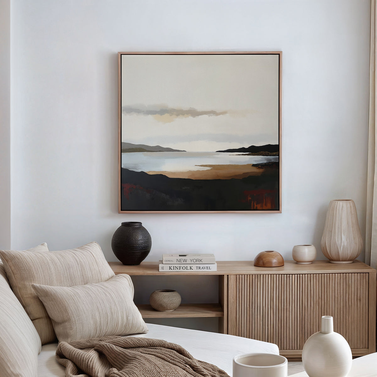 A neutral-toned living room features a beige sofa, cream pillows, a wooden sideboard with books and vases, and calming decor highlighted by the Nordic Waters Canvas Art - Square. Sheer curtains let in gentle natural light.