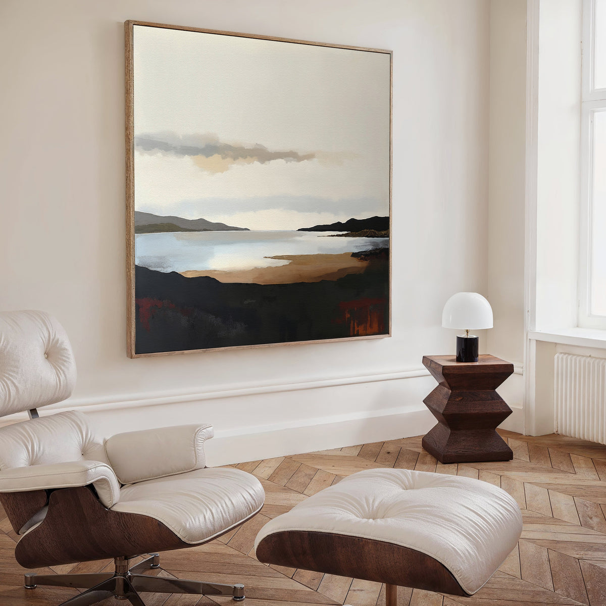 A minimalist living room features a white lounge chair and ottoman, a geometric wooden side table with a lamp, and the Nordic Waters Canvas Art - Square above light wood herringbone floors.