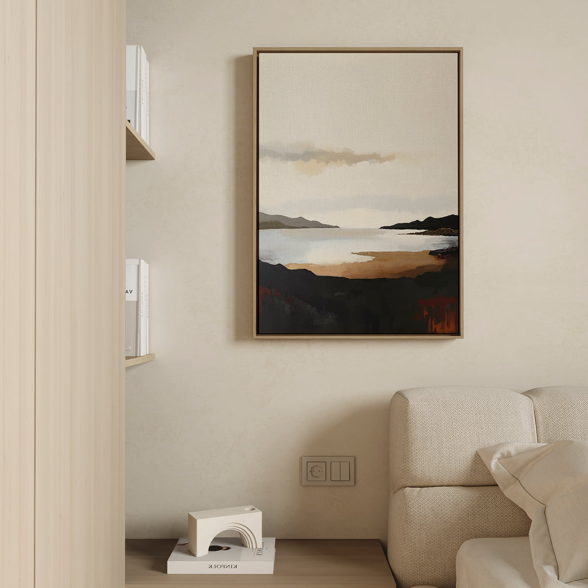 The Nordic Waters Canvas Art - Vertical features a coastal scene with dark hills and calm water in warm earth tones. Hanging on a beige wall, it complements a cream sofa and minimal shelf with books for a serene, stylish look.