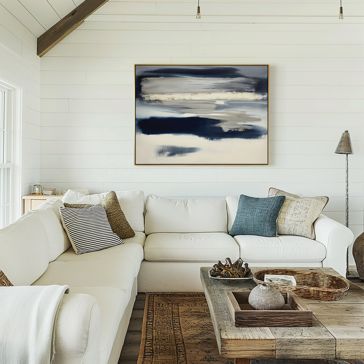 A cozy living room with a white sectional sofa, assorted throw pillows, a rustic wooden coffee table, and the Northern Tides Canvas Art - Horizontal in blue and white on a shiplap wall. Natural light brightens the minimalist palette.