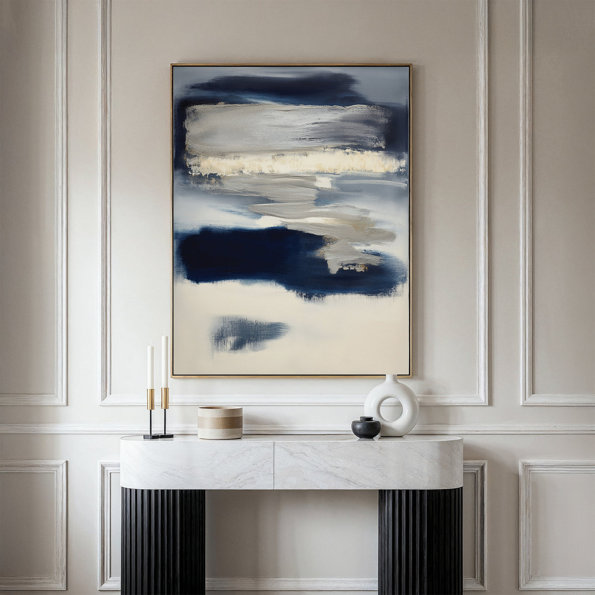 A modern console table stands against a paneled wall, topped by the Northern Tides Canvas Art - Vertical in navy, cream, and gray. Candles and sculptural decor in neutral tones complete the minimalist look.