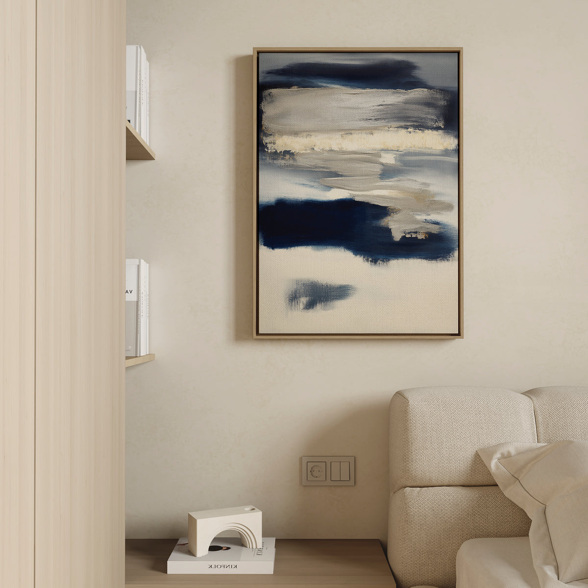 A modern living room corner with a cream sofa, minimalist decor, and the Northern Tides Canvas Art - Vertical featuring abstract navy blue, beige, and white brushstrokes displayed on a light-colored wall.