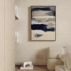 A modern living room corner with a cream sofa, minimalist decor, and the Northern Tides Canvas Art - Vertical featuring abstract navy blue, beige, and white brushstrokes displayed on a light-colored wall.